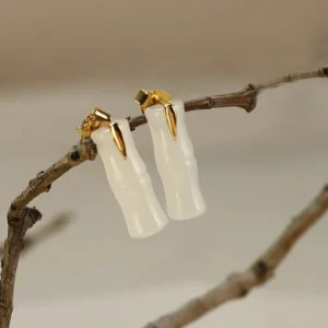 Hetian jade bamboo leaf stud earrings polished finish displayed on natural tree twigs, milky white jade with sterling silver posts