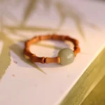 Hetian jade bamboo prosperity ring with light green jade bead and brown bamboo segments displayed on bamboo-leaf patterned book