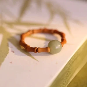 Hetian jade bamboo prosperity ring with light green jade bead and brown bamboo segments displayed on bamboo-leaf patterned book