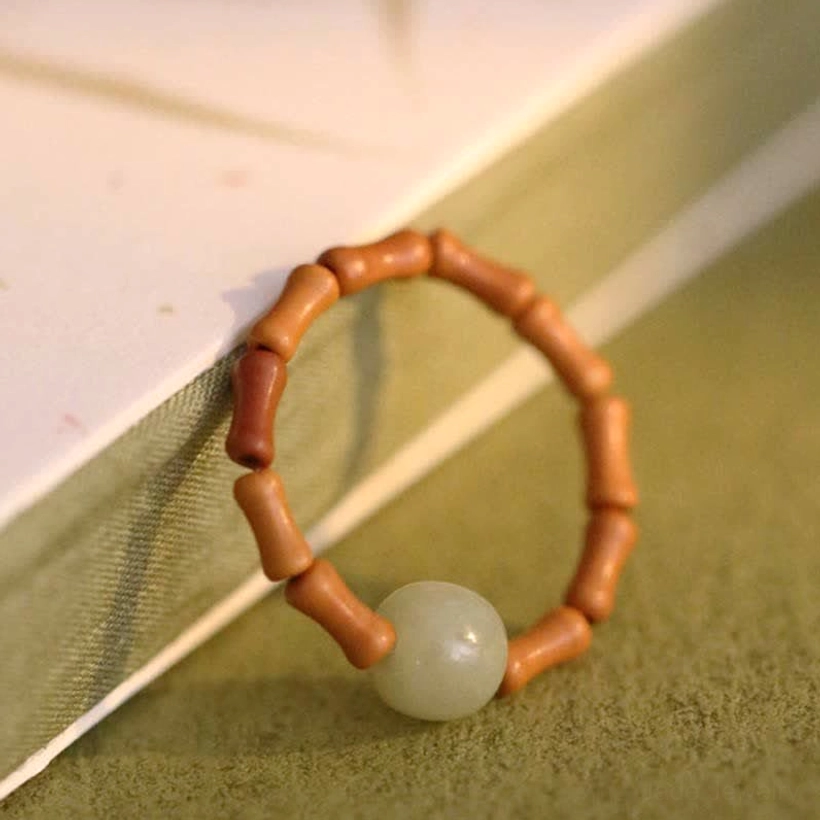 Close-up overhead view of adjustable hetian jade bamboo ring showing central light green jade bead on green fabric