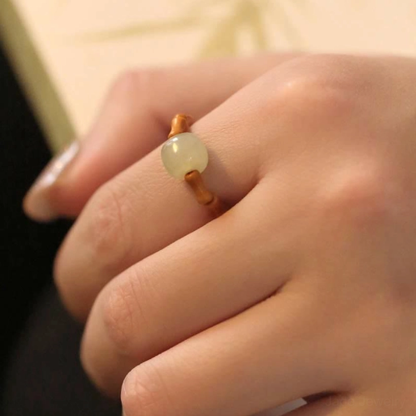 Hetian jade bamboo ring worn on middle finger in three-quarter view with book backdrop