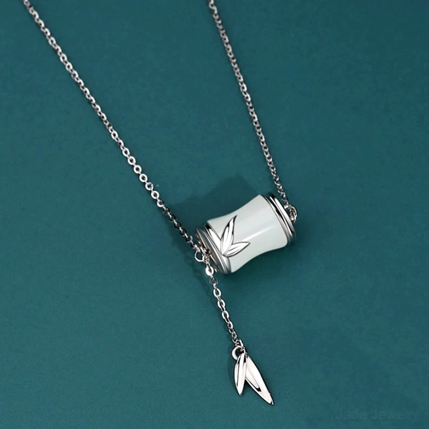 Sterling silver Hetian white jade bamboo Y-lariat necklace featuring handcrafted jade bamboo charm and silver leaf tassel pendant on dark teal studio background, showing fine metalwork detail