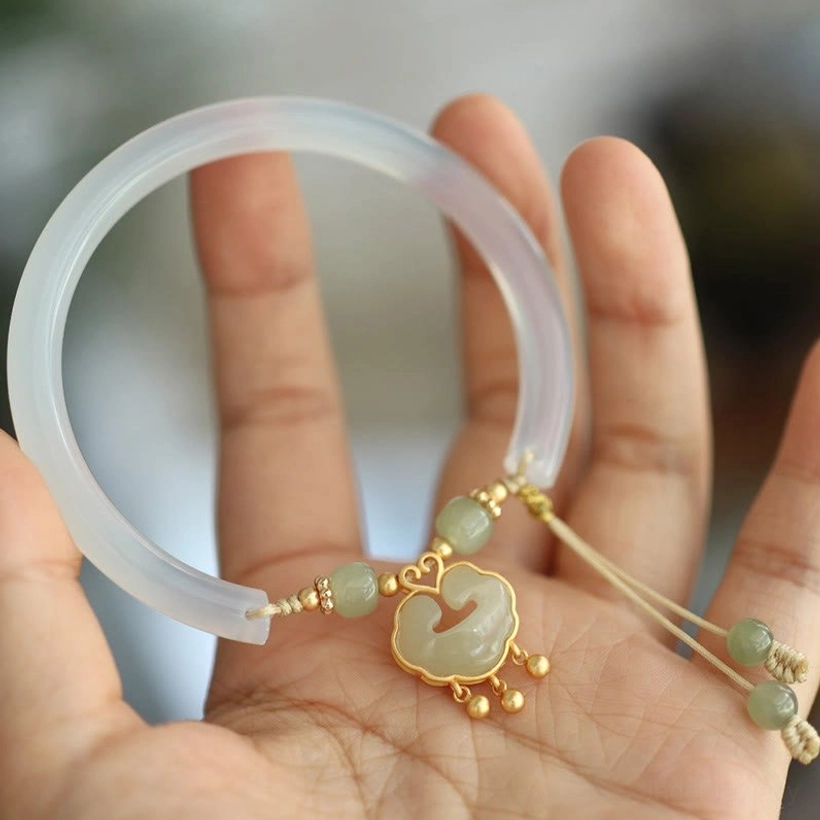 Hand-held top view of hetian jade bangle bracelet in palm, displaying translucent chalcedony band, gold hardware, and jade bead tassels
