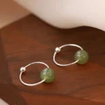 Green Hetian jade bead sterling silver hoop earrings - top-down flat lay showcasing minimalist open hoop design with polished jade beads on wooden display