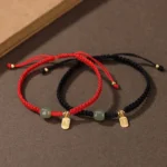 Red and black Hetian jade blessing bracelets with sterling silver fu charms displayed flat lay on brown table