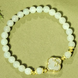 Close-up of light green jade beads with bamboo charm and gold metal hardware on olive green backdrop