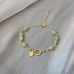 Natural Hetian jade beaded bracelet with 14K gold-filled chain and toggle clasp on grey fabric background