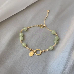 Natural Hetian jade beaded bracelet with 14K gold-filled chain and toggle clasp on grey fabric background