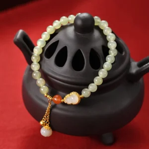 Three-quarter view of green Hetian jade beaded bracelet with white gourd charm and gold filigree on red incense burner background