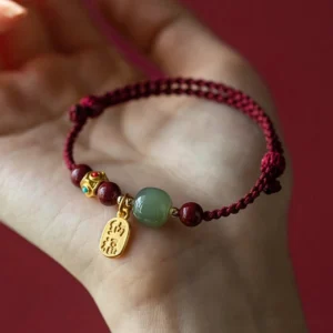 Hetian jade protection bracelet worn on palm, showing enamel-inlaid gold fortune charm and braided red string design
