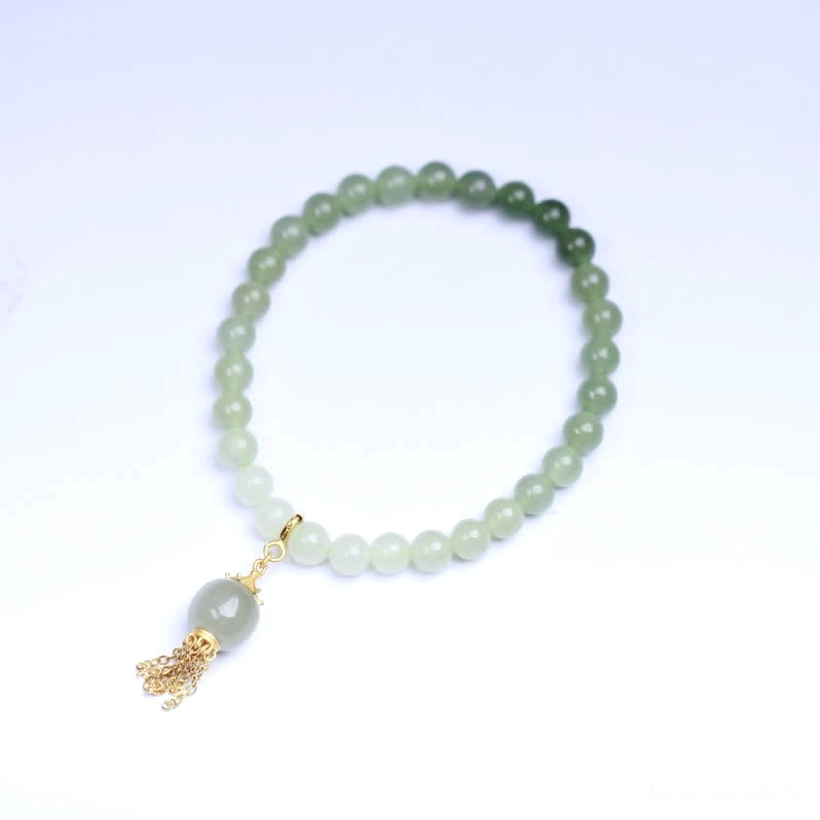 Hetian jade beaded bracelet flat lay on plain light background, ombre deep-to-light green jade beads with gold tassel pendant