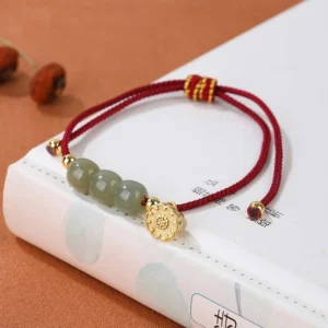 Red rope Hetian jade bracelet with green jade beads and gold lotus pod charm displayed on Chinese poetry book