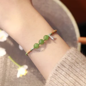 Green hetian jade beaded bracelet with silver bamboo charm worn on wrist over knitted sweater showing side profile and fit