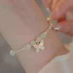 Hetian jade butterfly charm bracelet worn on wrist with silver beaded chain and pale jade beads on sheer fabric