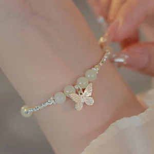 Hetian jade butterfly charm bracelet worn on wrist with silver beaded chain and pale jade beads on sheer fabric