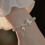 Hetian jade butterfly adjustable chain bracelet worn on wrist with vintage ruffled sleeve background, showing gold-toned hardware and dangling jade beads