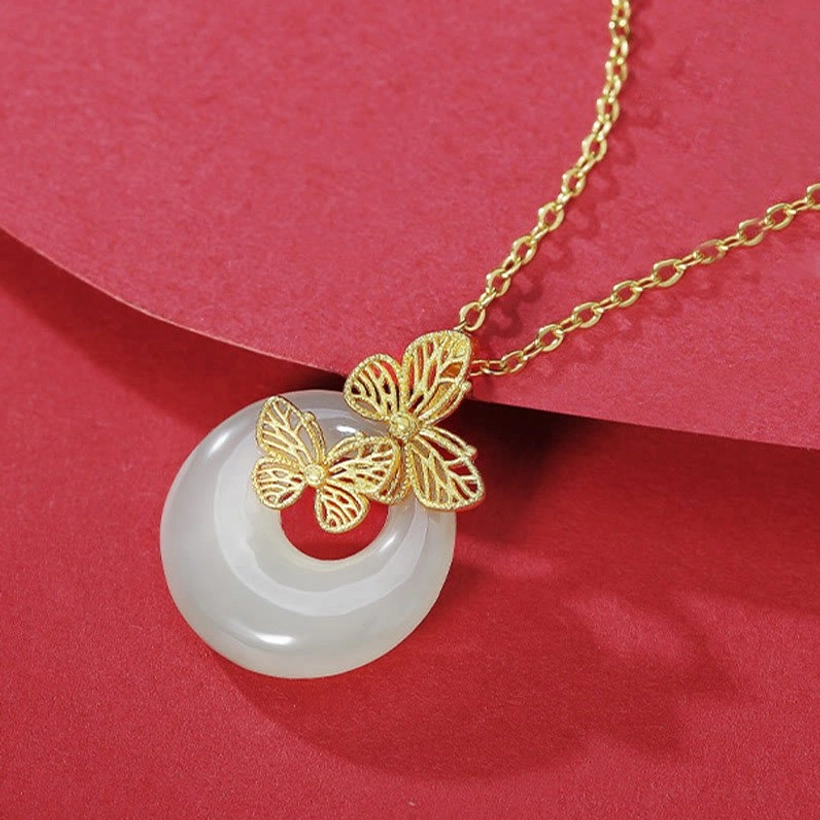 Double butterfly jade pendant necklace displayed on red fabric backdrop, showing detailed gold chain and jade pendant from an oblique angle