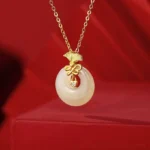 Hetian jade carnation pendant with gold-plated ginkgo mount and cubic zirconia details on red satin background