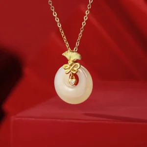 Hetian jade carnation pendant with gold-plated ginkgo mount and cubic zirconia details on red satin background