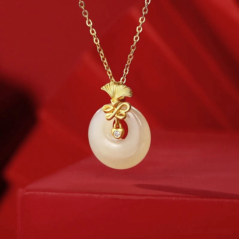 Hetian jade carnation pendant with gold-plated ginkgo mount and cubic zirconia details on red satin background