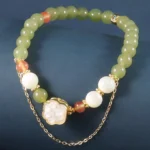 Hetian jade cat paw prosperity bracelet with tridacna stone beads on dark blue background, flat lay view showing mixed green white and peach accent beads with gold-toned cat paw charm