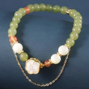 Hetian jade cat paw prosperity bracelet with tridacna stone beads on dark blue background, flat lay view showing mixed green white and peach accent beads with gold-toned cat paw charm