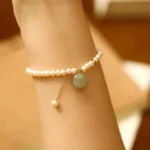 Hetian jade cat paw charm with freshwater pearl bracelet worn on wrist, close-up side view showing delicate gold clasp and dangling pearl accent