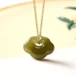 Hetian jade cloud lock pendant necklace with light celadon green jade and sterling silver or copper chain in flat lay on natural background