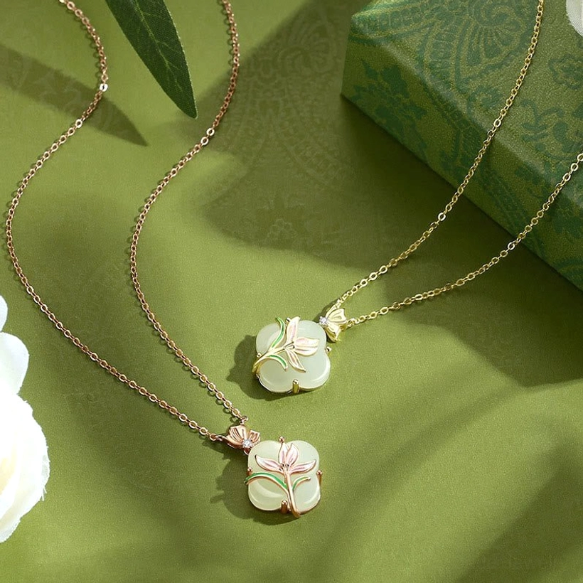 Two matching Hetian jade four leaf clover necklaces with gold chains displayed flat lay with gift box background