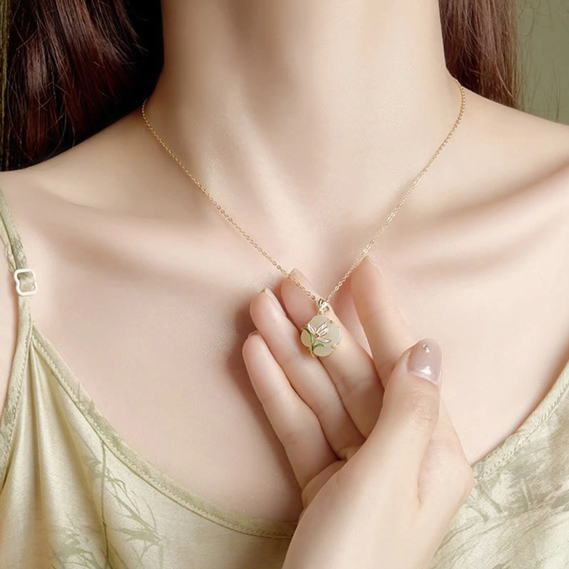 Woman wearing delicate Hetian jade four leaf clover necklace with gold chain close-up on neck and hands