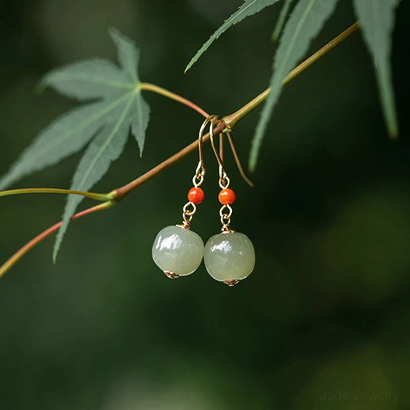 Jade drop earrings with red agate hanging on outdoor maple twig branch in natural daylight