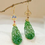 Hetian jade enamel dangle earrings with blue cloisonné flower top, red gem accent, and carved green jade pendant hanging on decorative twig