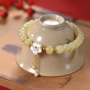 Hetian jade white flower lucky bracelet with pearl tassel overhead view on ceramic holder with wooden table