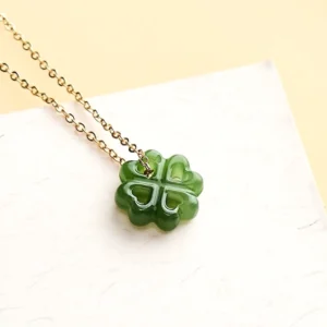 Green jade four leaf clover charm showing fine carving details with delicate gold chain on white background
