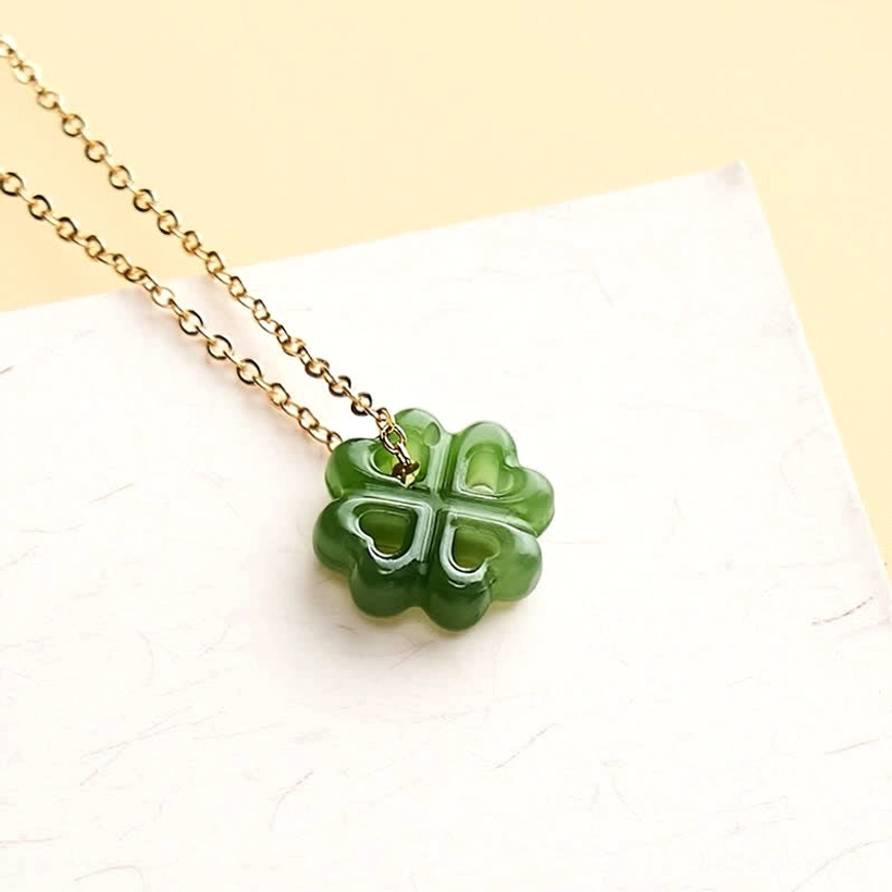 Green jade four leaf clover charm showing fine carving details with delicate gold chain on white background