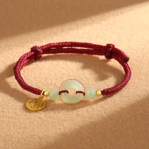 Hetian jade peace buckle fu character charm bracelet with red braided cord and 925 sterling silver pendant on brown fabric