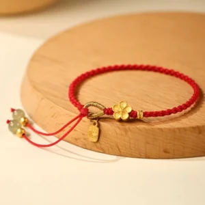 Hetian jade fu character peach blossom bracelet with red string and gold charms displayed on wooden coaster in flat lay