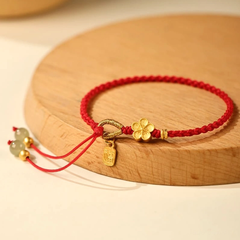 Hetian jade fu character peach blossom bracelet with red string and gold charms displayed on wooden coaster in flat lay