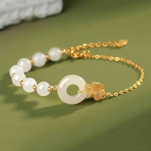 Hetian white jade ginkgo peace buckle bracelet with 925 sterling silver chain, side flat lay view on green textile background