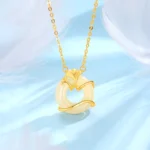Gold-plated Hetian jade ginkgo leaf peace buckle necklace pendant with creamy white jade center, flat lay on light blue feather background