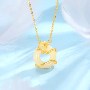 Gold-plated Hetian jade ginkgo leaf peace buckle necklace pendant with creamy white jade center, flat lay on light blue feather background