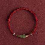 Hetian jade gourd bracelet with dark red braided cord and silver beads on dark fabric background