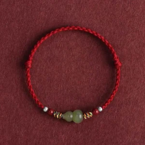 Hetian jade gourd bracelet with dark red braided cord and silver beads on dark fabric background