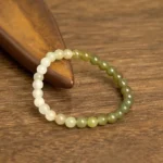 Hetian jade gradient bracelet with ombre beads transitioning from cream to green, displayed on wooden desktop