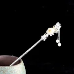 Hetian white jade flower hairpin with 925 sterling silver inserted in ceramic vessel, showing twisted silver shaft and beaded tassel detail