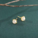 Hetian jade heart stud earrings with gold-plated sterling silver posts, overhead flat lay view on green fabric backdrop showcasing creamy white jade with floral metal claw setting