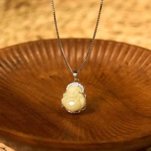 Yellow Hetian jade Laughing Buddha pendant necklace with silver chain and rhinestone frame, top-down view on wooden background