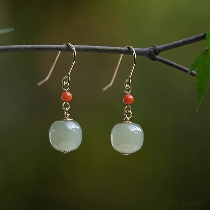 Hetian jade light green drop earrings with red agate beads and gold ear hooks displayed on outdoor twig with green foliage