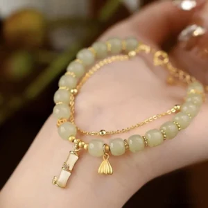 Front close-up of Hetian jade prosperity bracelet on wrist – green jade beads with lotus and bamboo gold charms, soft indoor lighting