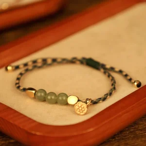 Hetian jade lotus bracelet with green jade beads and gold charm displayed on wooden tray, flat lay top view